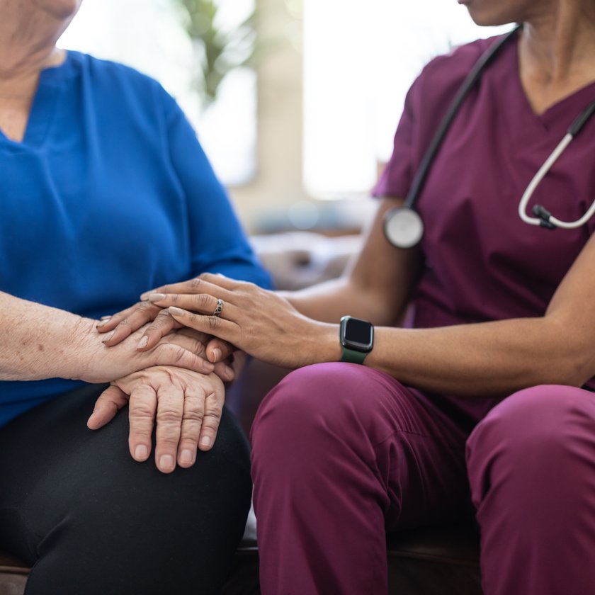 A nurse in scrubs holding an older patient's hands